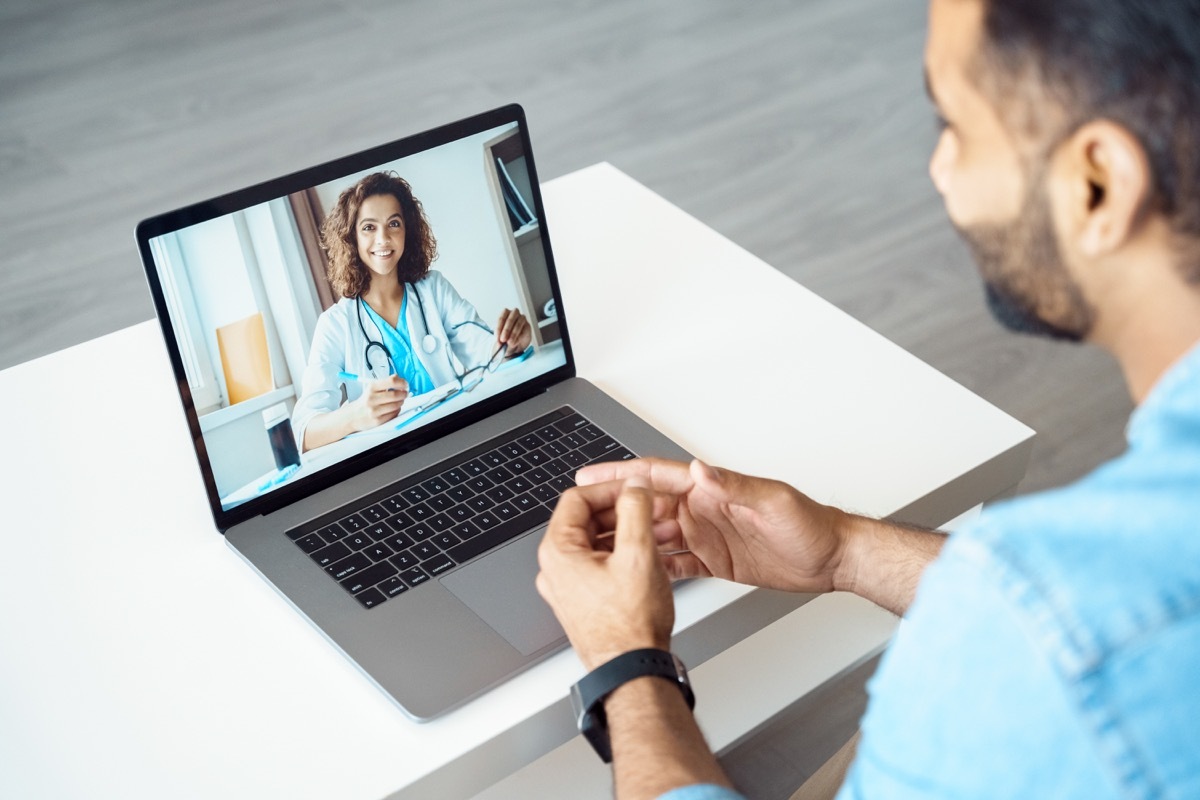 View over male client shoulder sit at desk receive medical consultation online from female doctor.
