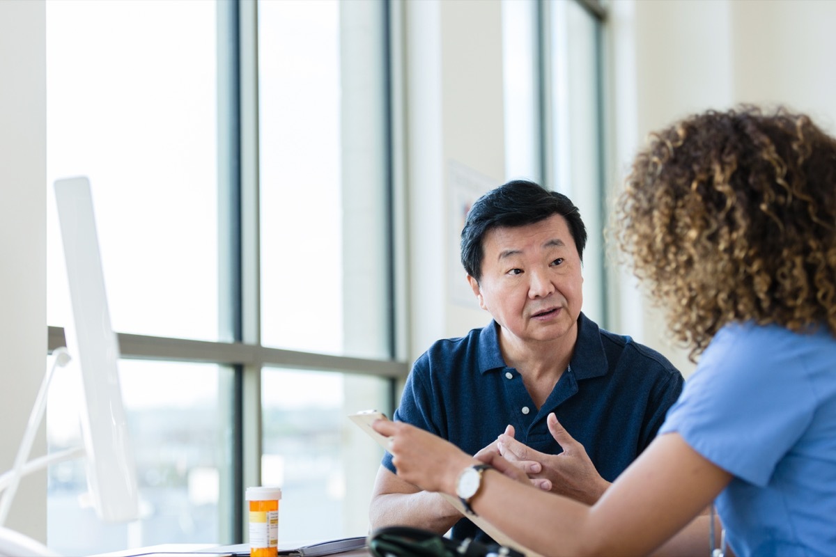 Serious senior man listens as a female healthcare professional discusses a medical diagnosis and treatment. A prescription medication container is sitting on the desk.