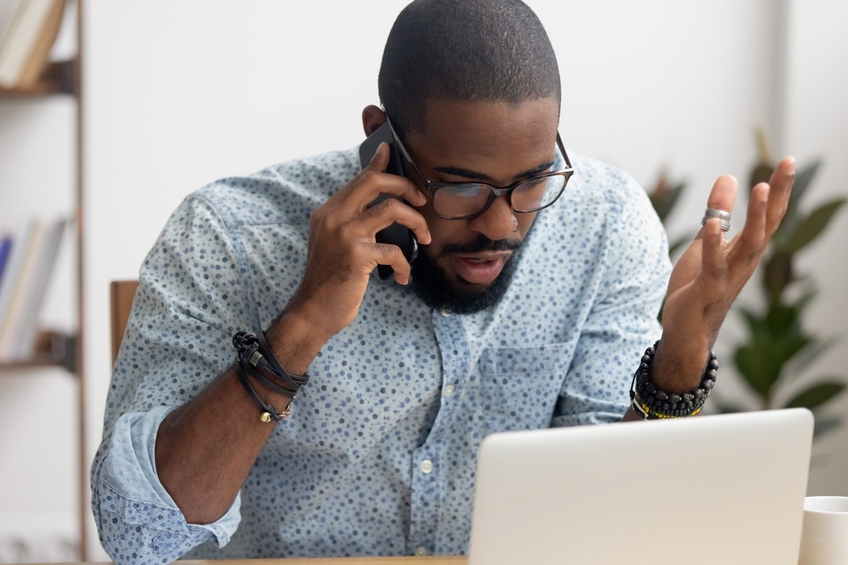 businessman talking on cellphone looking at laptop in office