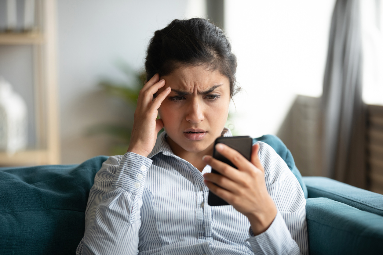 A young woman looks at her smartphone with a concerned look on her face.