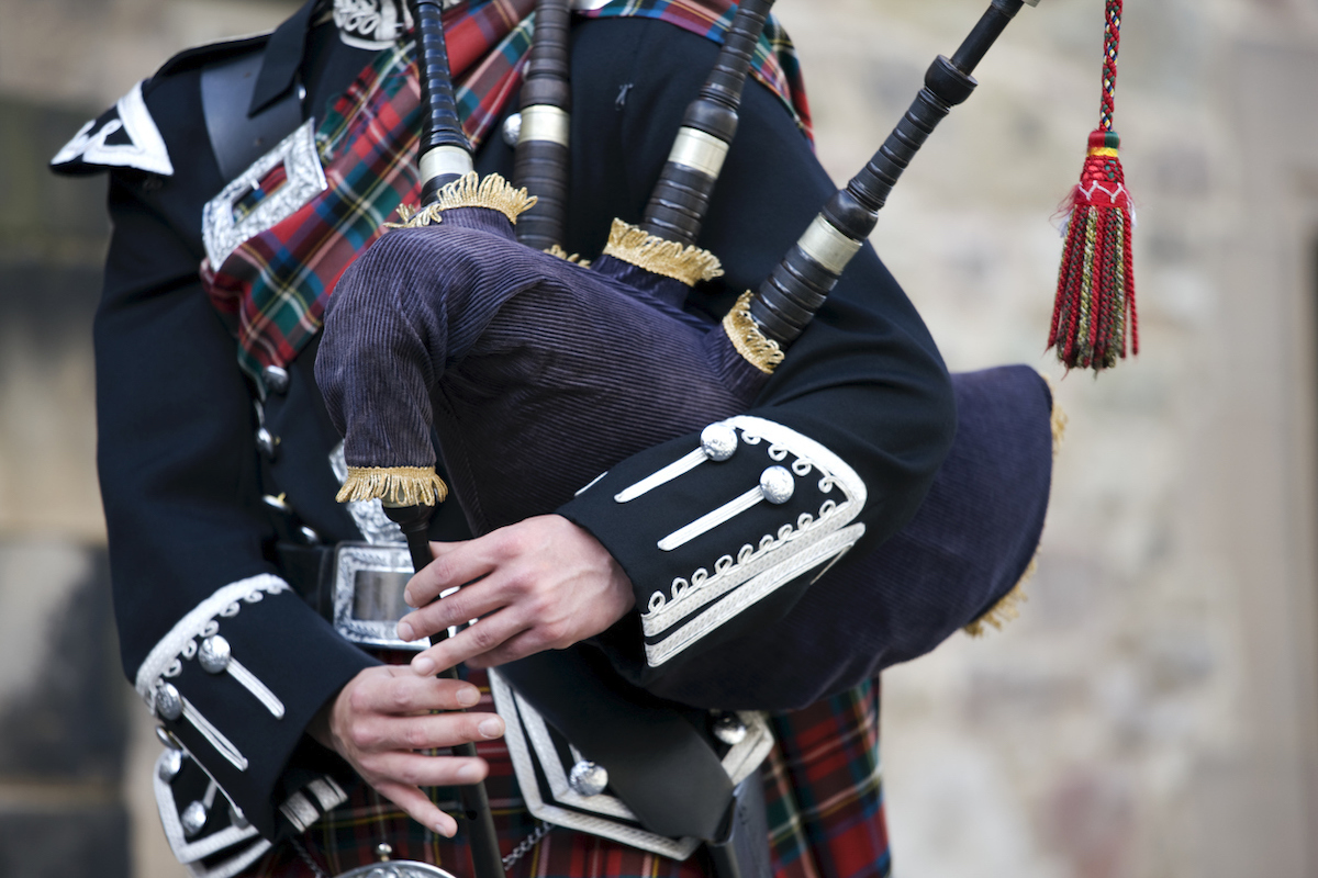 Close up of the hands of a Scottish bagpiper clad in a traditional scottish tartan playing the Scottish bagpipe