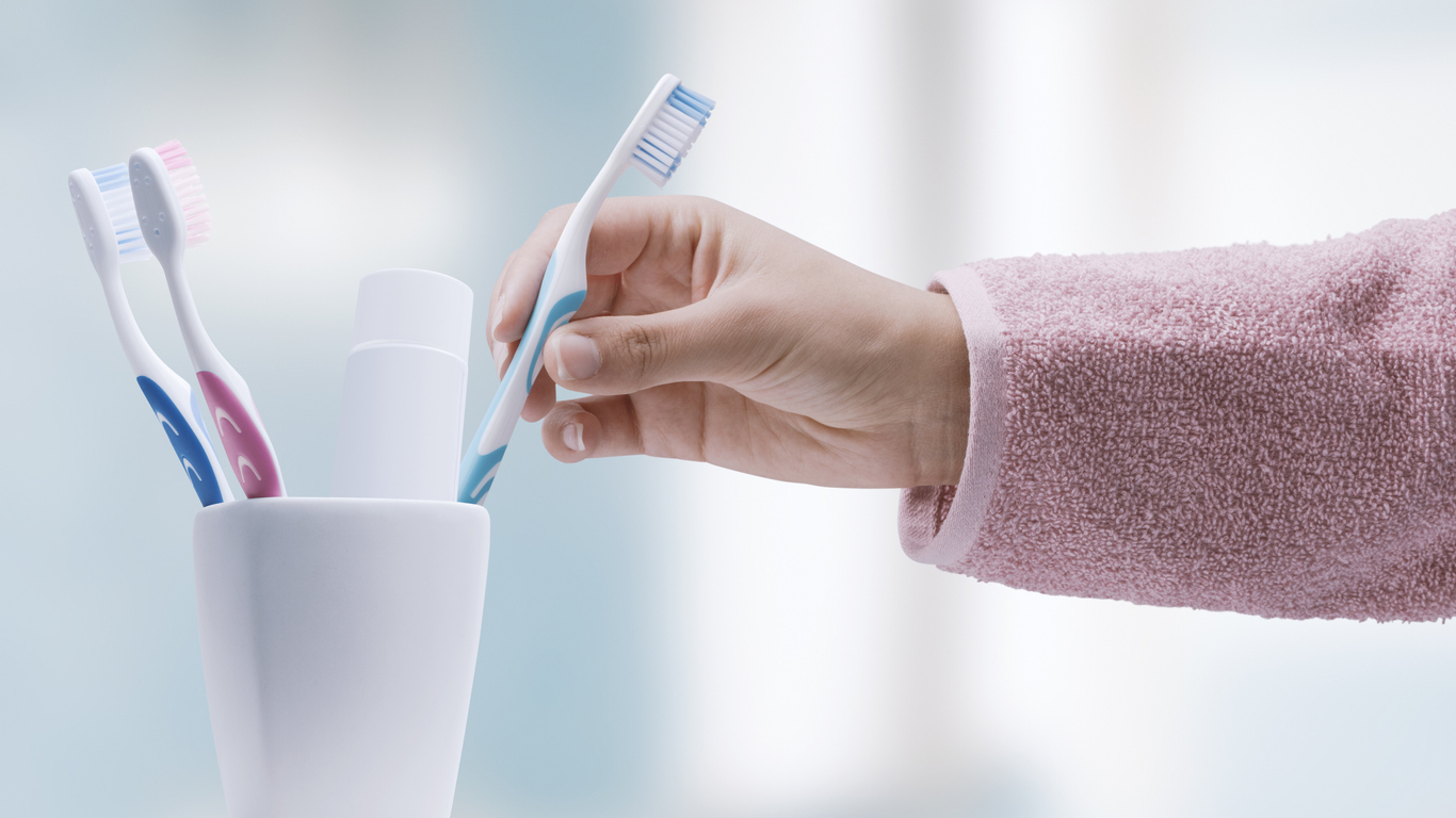 Hand holding a toothbrush over a cup with other toothbrushes in it.
