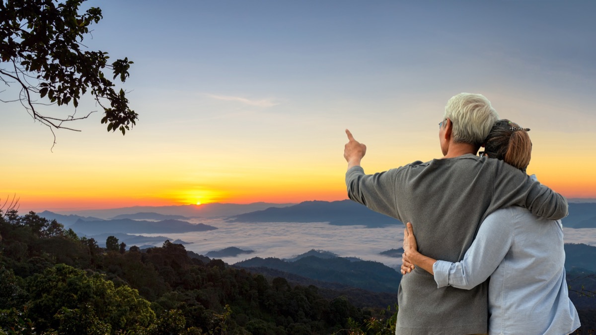 An elderly couple looks out at the sunset.