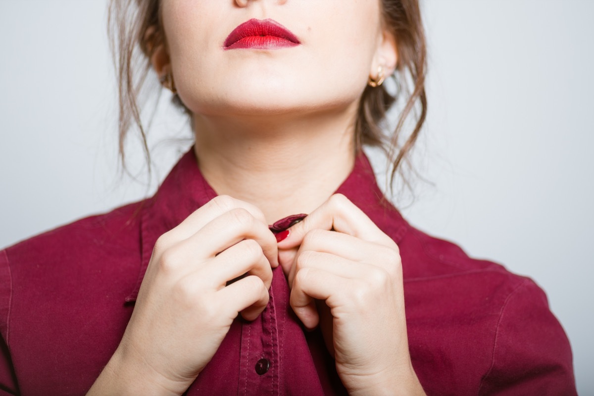 Woman buttoning her shirt, isolated on a gray background