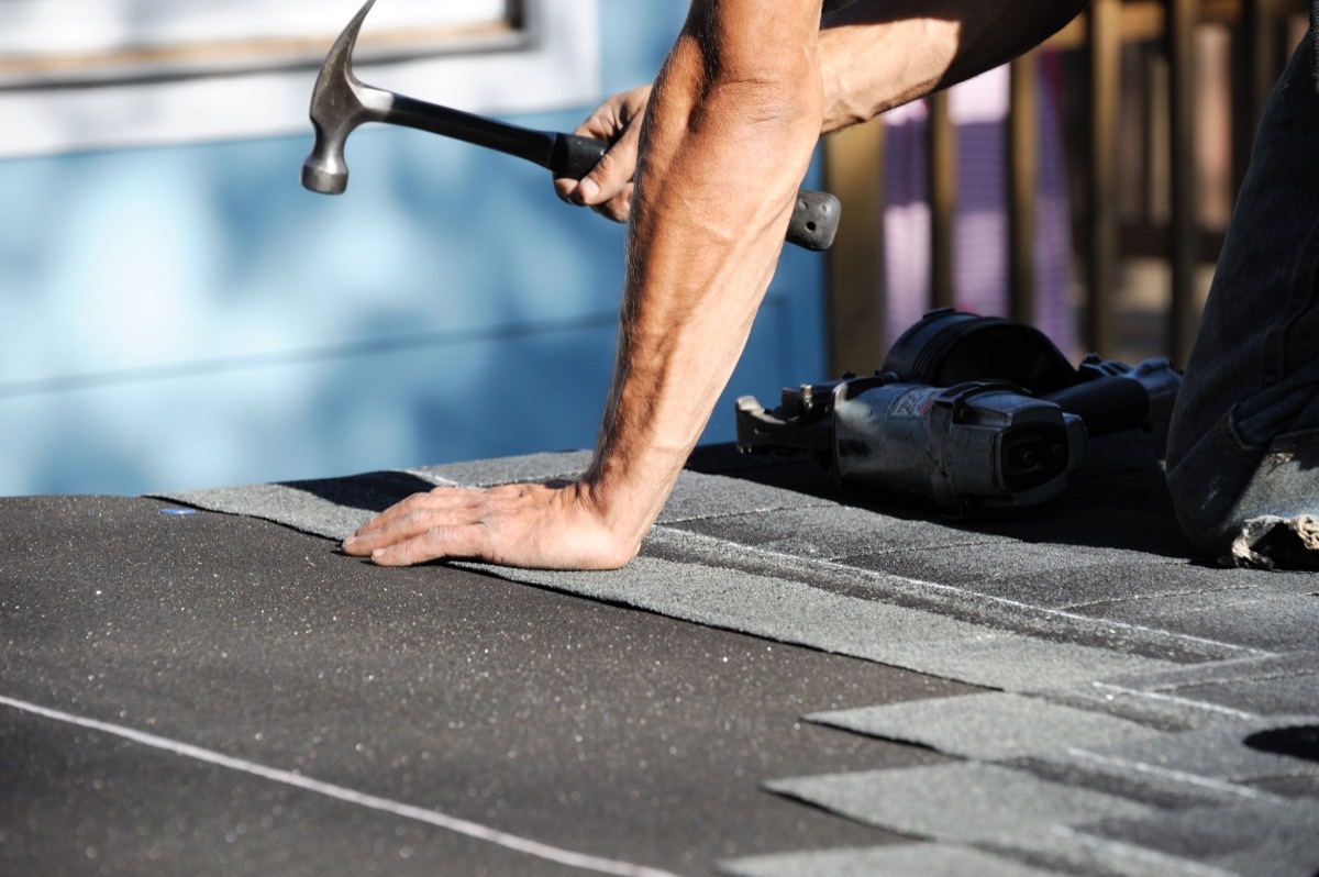 white man hammering shingles onto roof