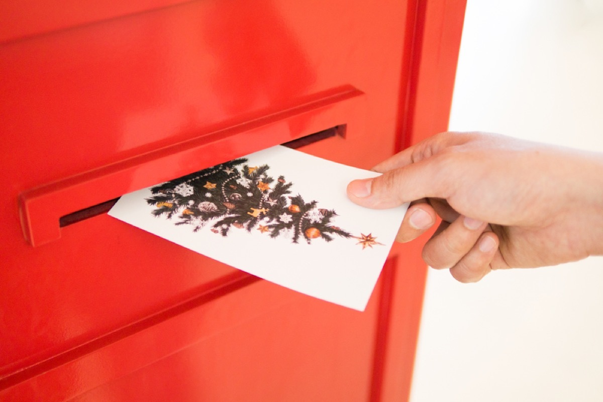 white hand putting christmas card through slot in red door
