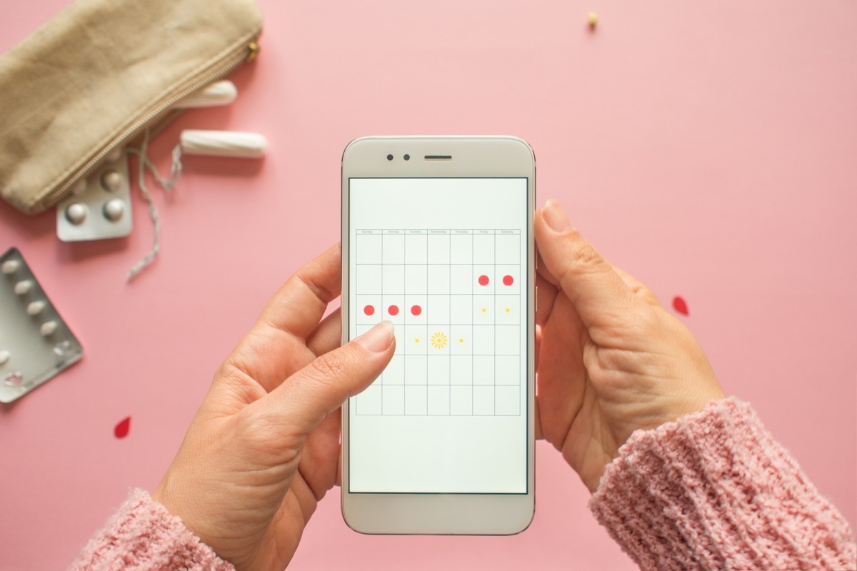 Woman tracking her period on phone, pink background