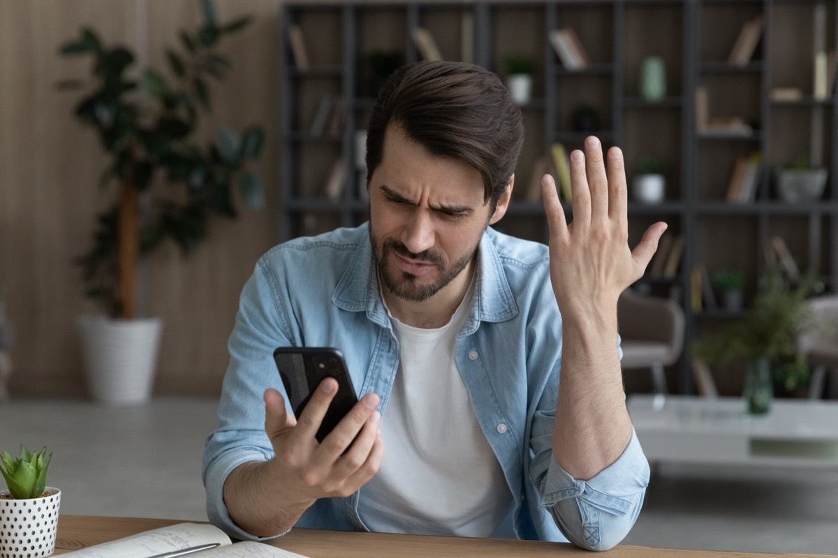 man putting his hand up in annoyance while looking at his phone