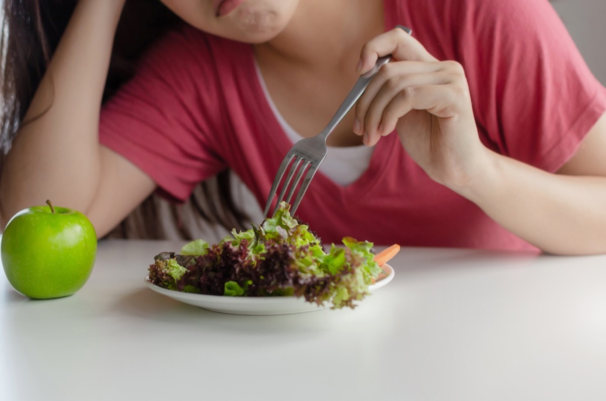 close up of young woman's frown as she picks at a salad with her fork