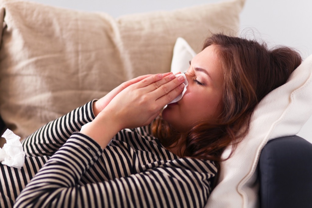 woman sneezing on couch, contagious conditions