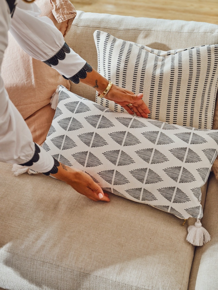 hands putting gray and white throw pillow on couch