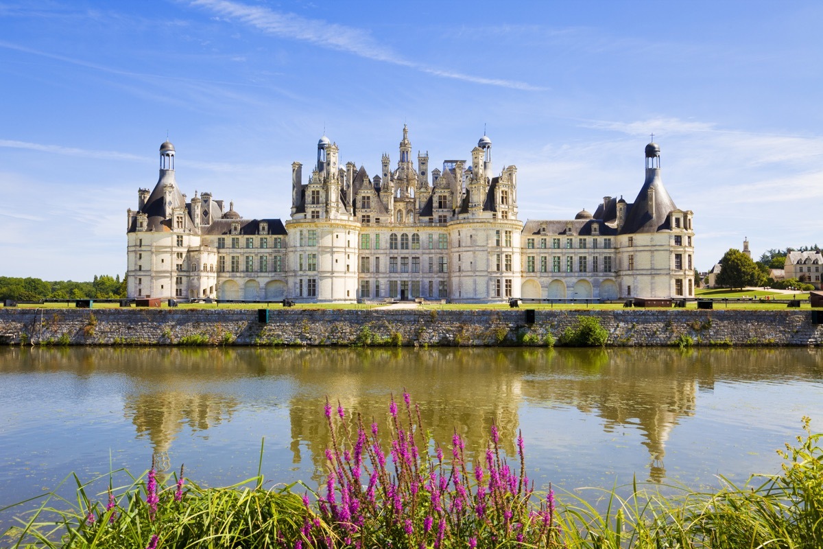 Great panoramic of Chambord Chateau reflected in the canal in a summer day with blue sky.