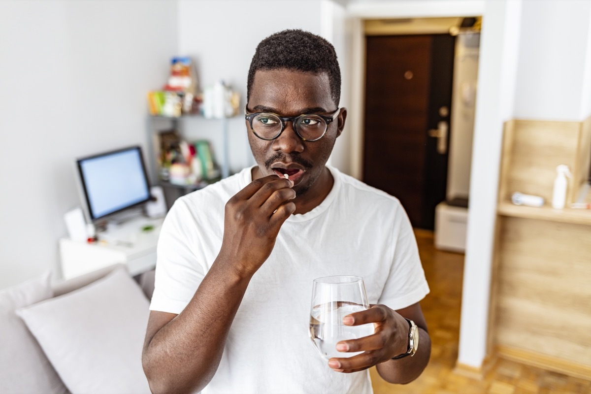 Shot of a young man taking medication while standing at home during the day.