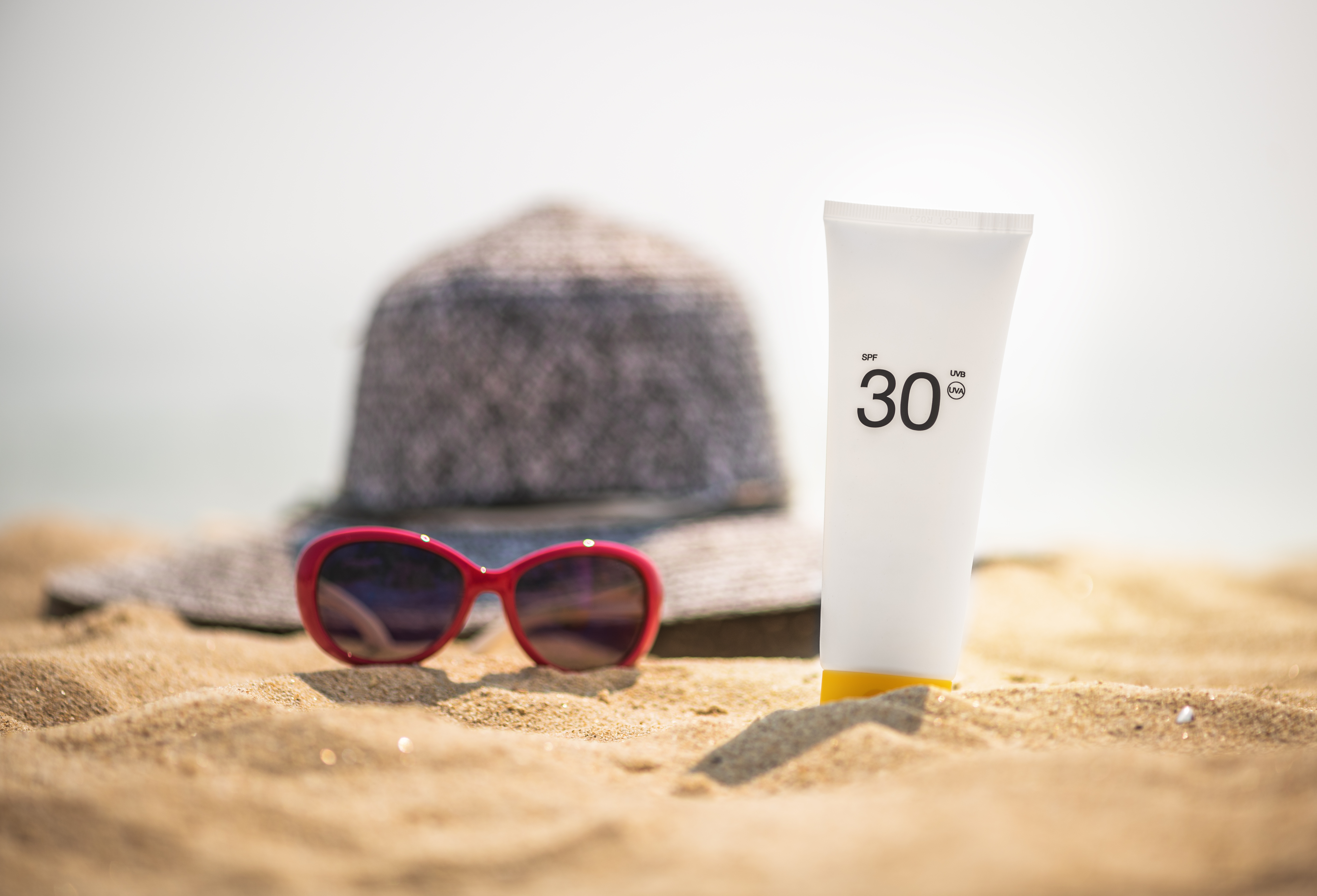 sunglasses and SPF suncreen sitting on a beach, healthy-skin-after-40-spf